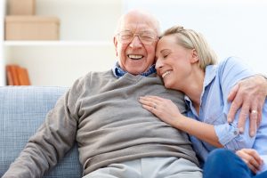 Loving senior man embracing his daughter while sitting on sofa smiling